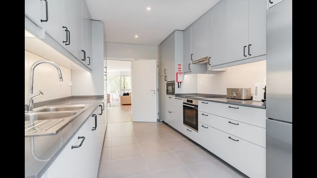Una cocina moderna y luminosa con gabinetes blancos y electrodomésticos de acero inoxidable.