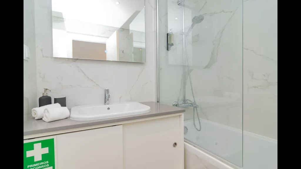 Un baño luminoso con lavabo, espejo y ducha de cristal.