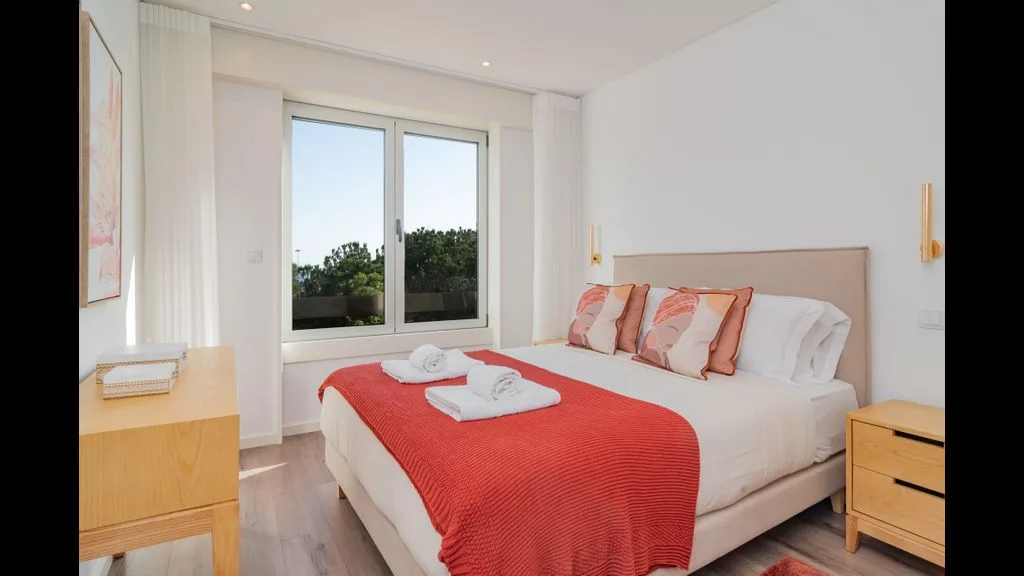 Un dormitorio luminoso con una cama vestida de blanco y una colcha roja.