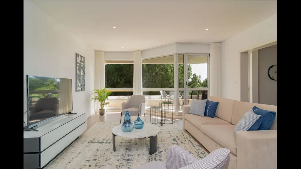 Una sala luminosa con asientos, un televisor y amplias ventanas.