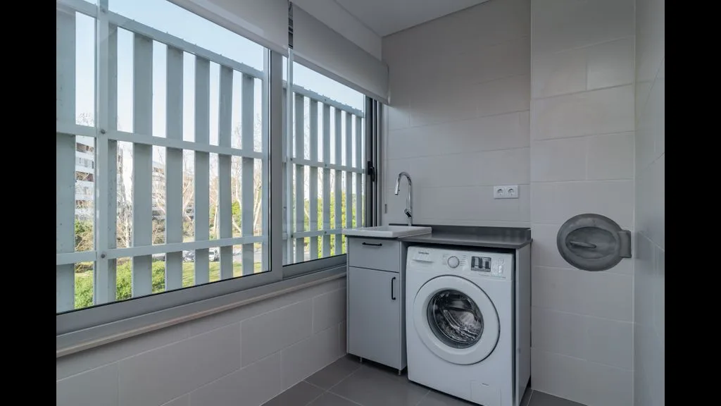 Zona de lavandería con una lavadora junto a una ventana amplia.