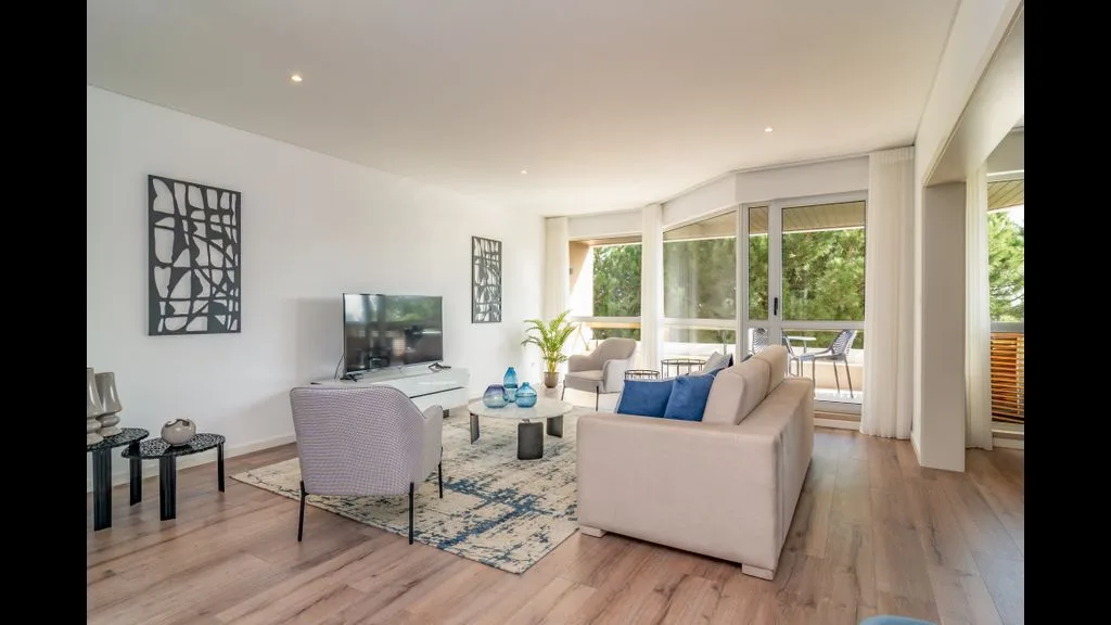 Bright living room with seating, a television, and large windows.
