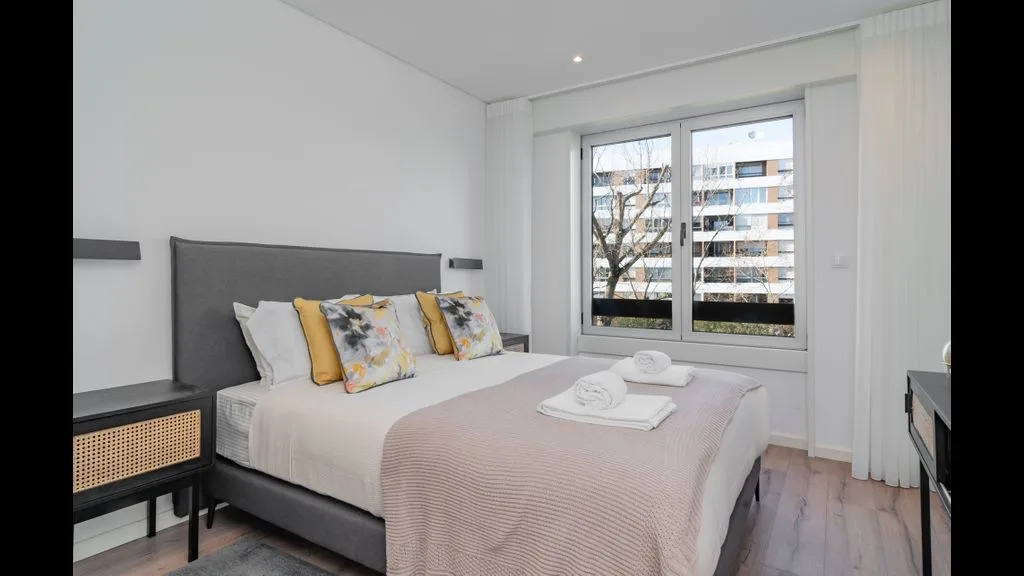 Un dormitorio luminoso con una cama tendida junto a una ventana grande.