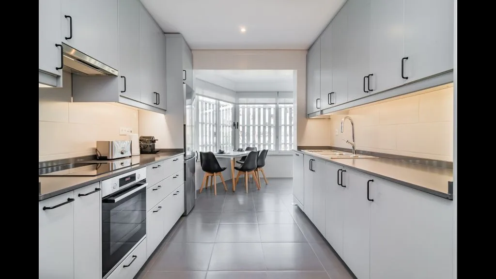 Una cocina moderna con gabinetes blancos, encimeras y un pequeño comedor.