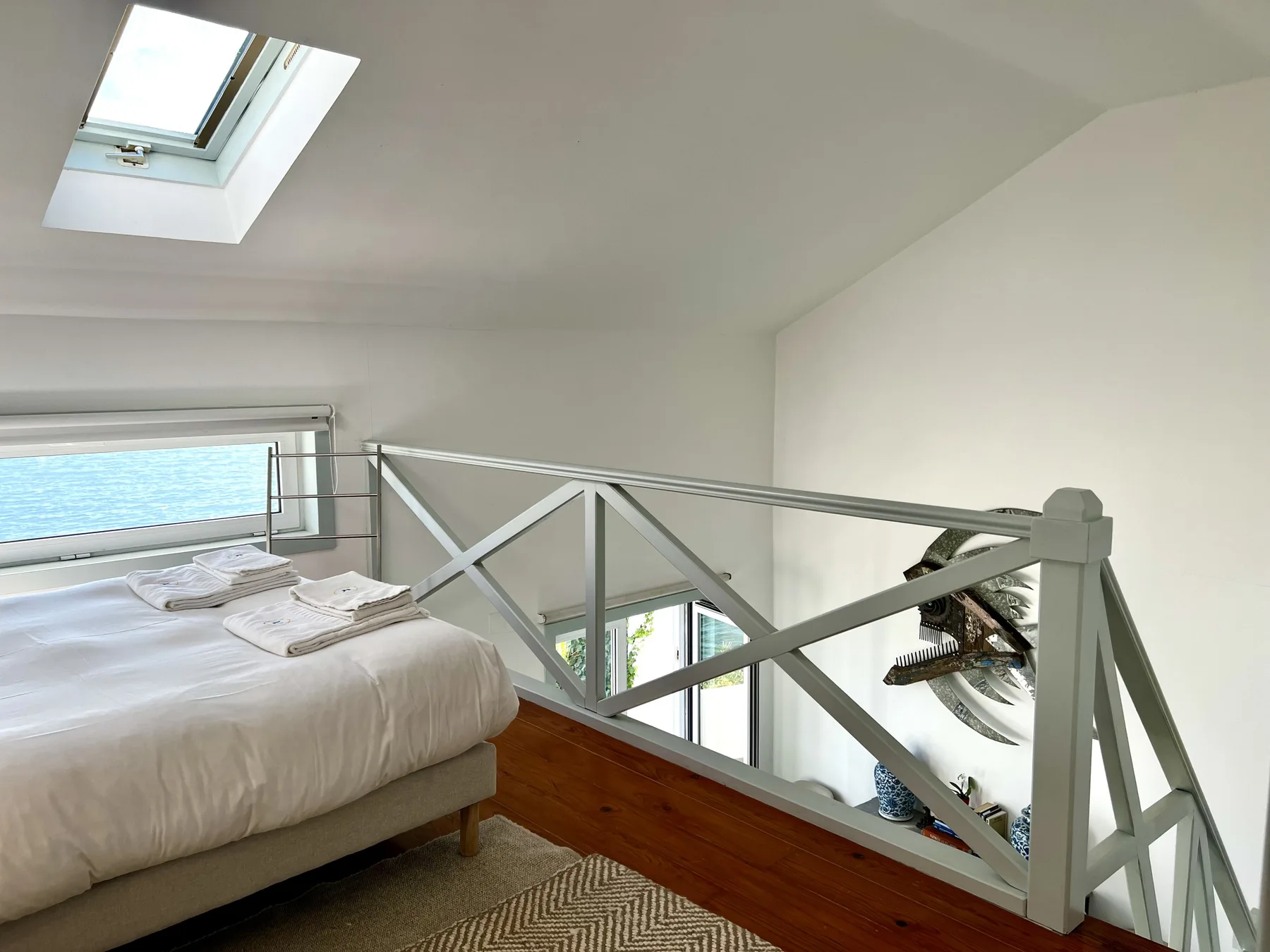 A bright bedroom with a skylight and a bed beside a railing.