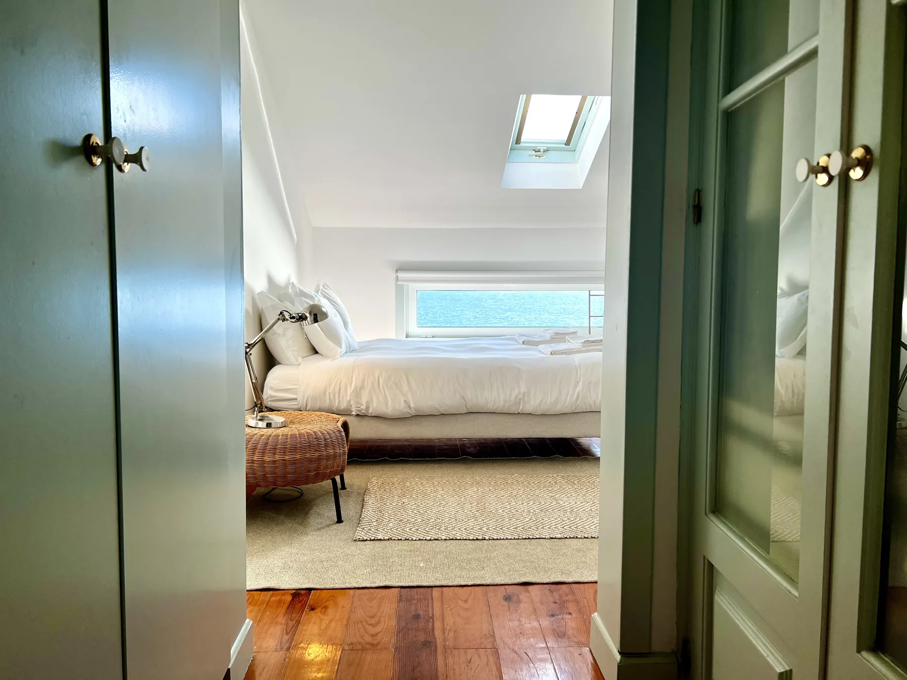 A bedroom with a bed beneath a skylight and a window overlooking the water.