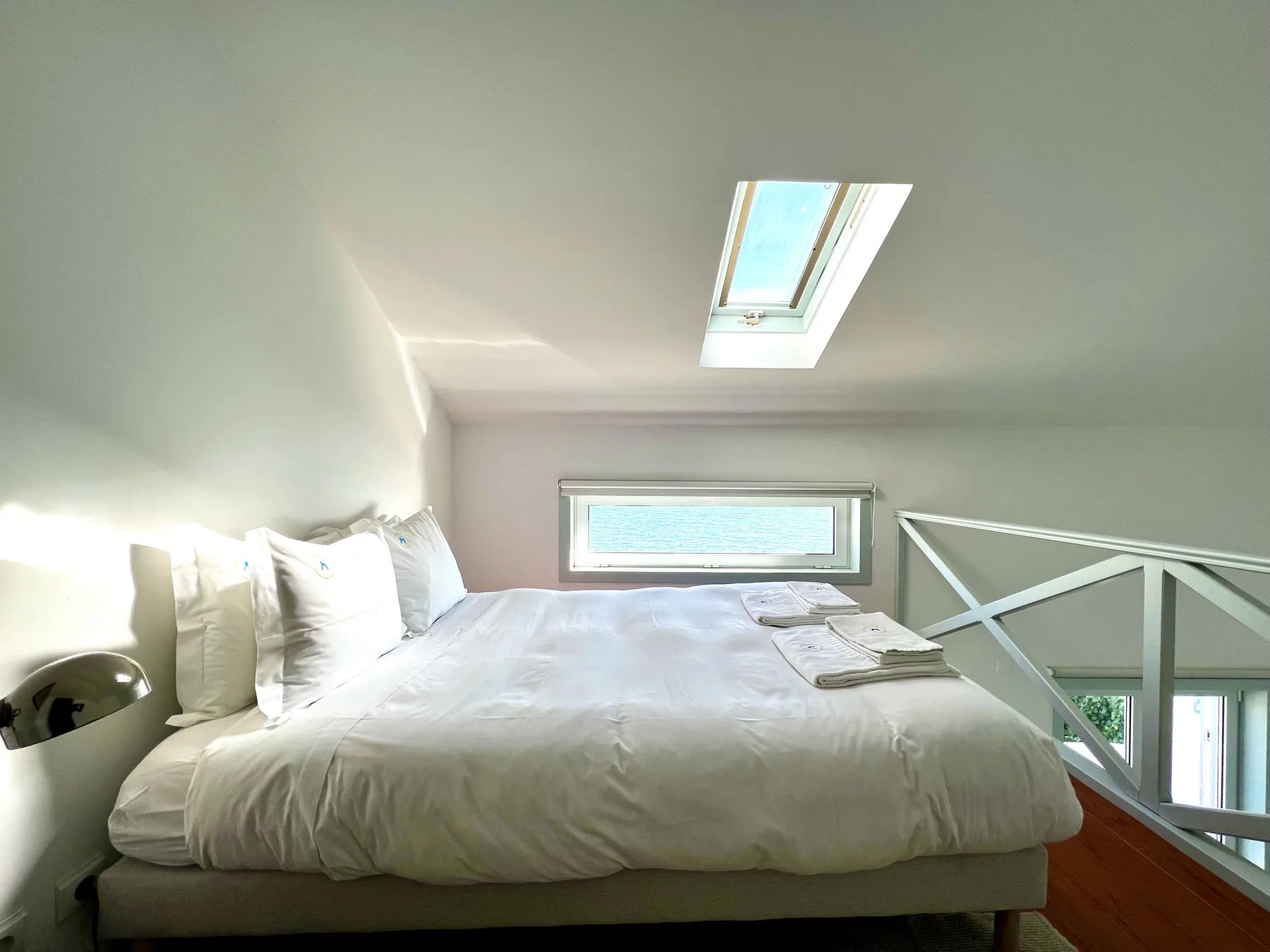 A bedroom with a bed beneath a skylight and a low window.