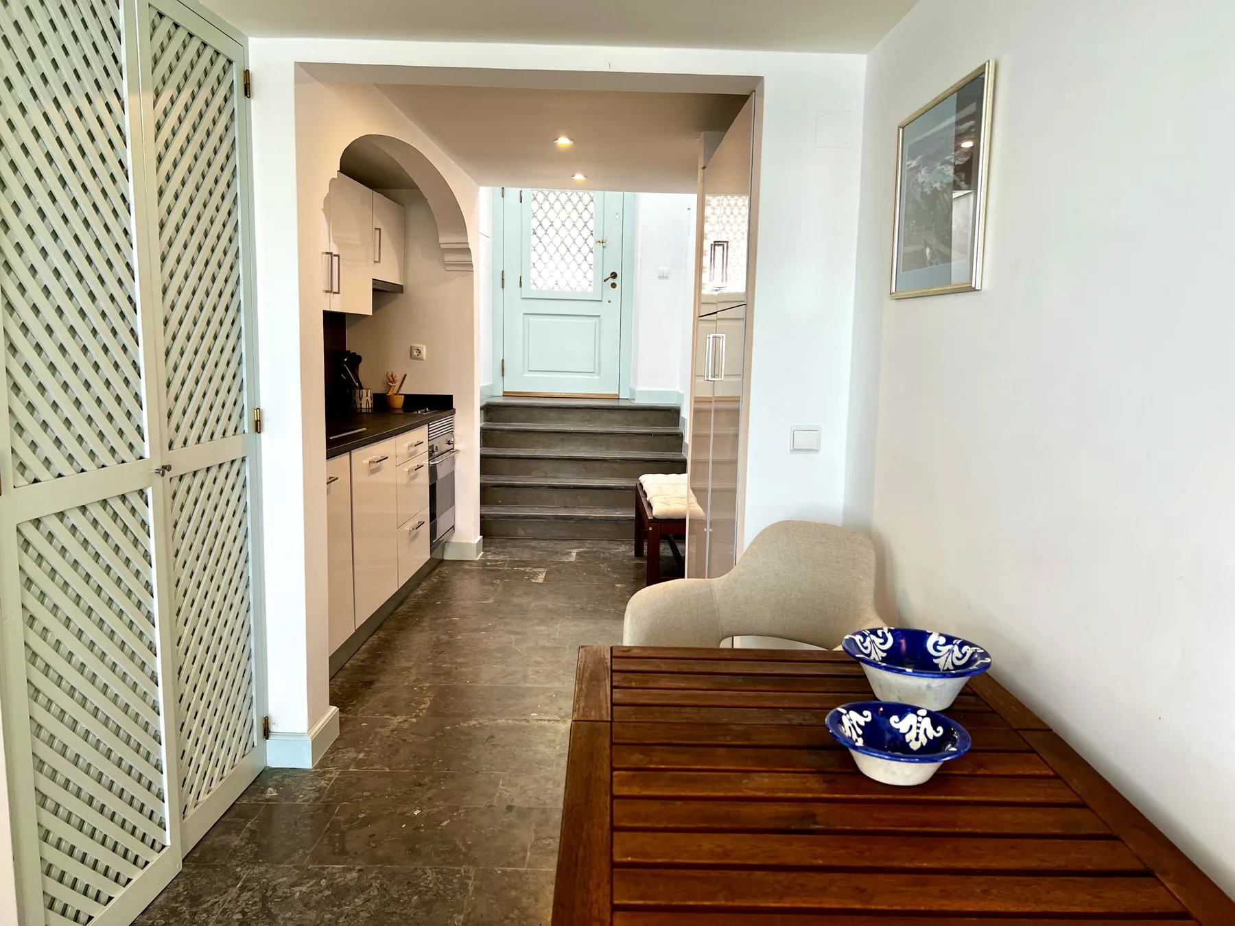 A narrow interior hallway with a small kitchenette and a wooden table in the foreground.