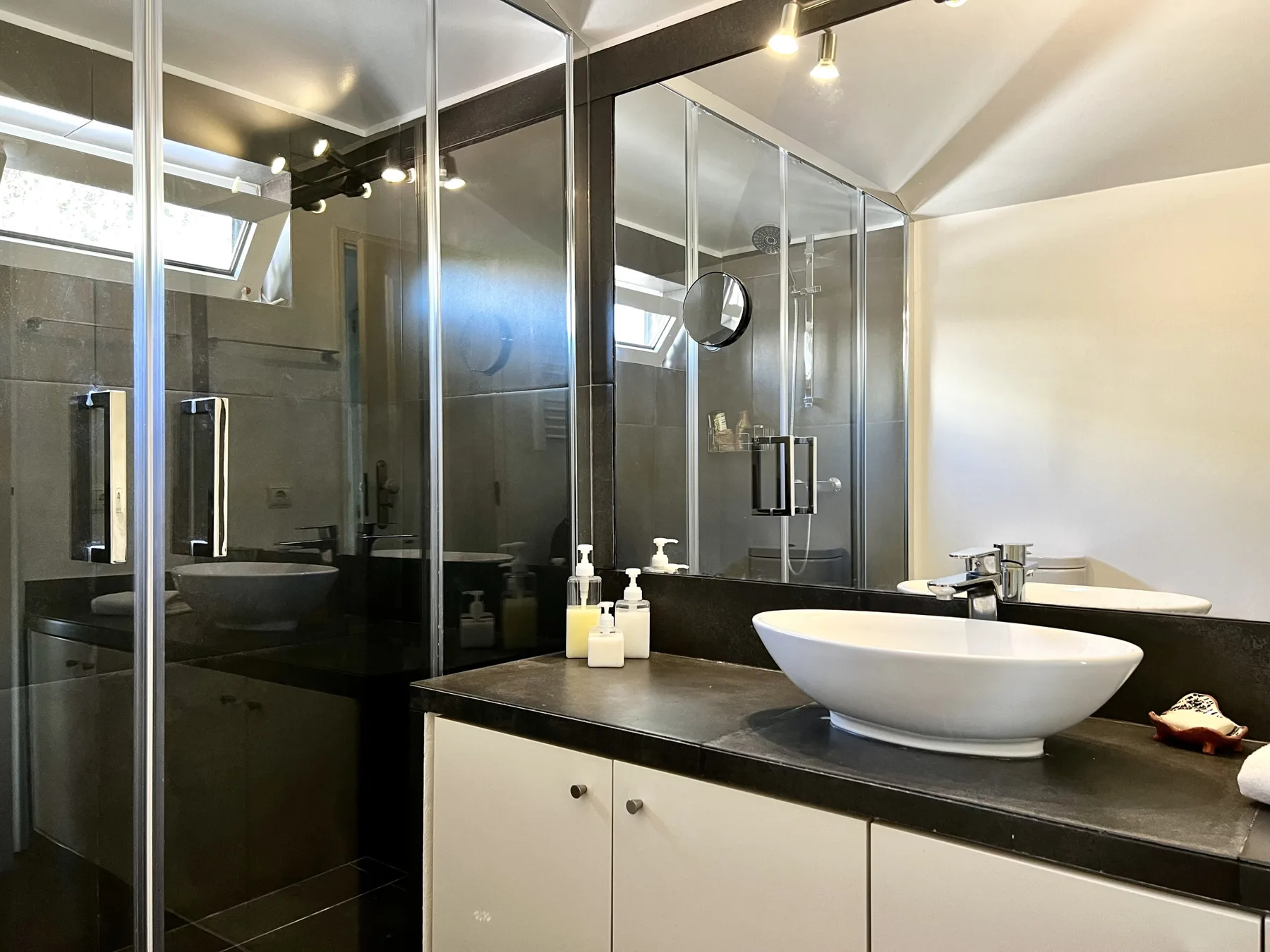 A modern bathroom with glass showers and a vessel sink on a dark counter.