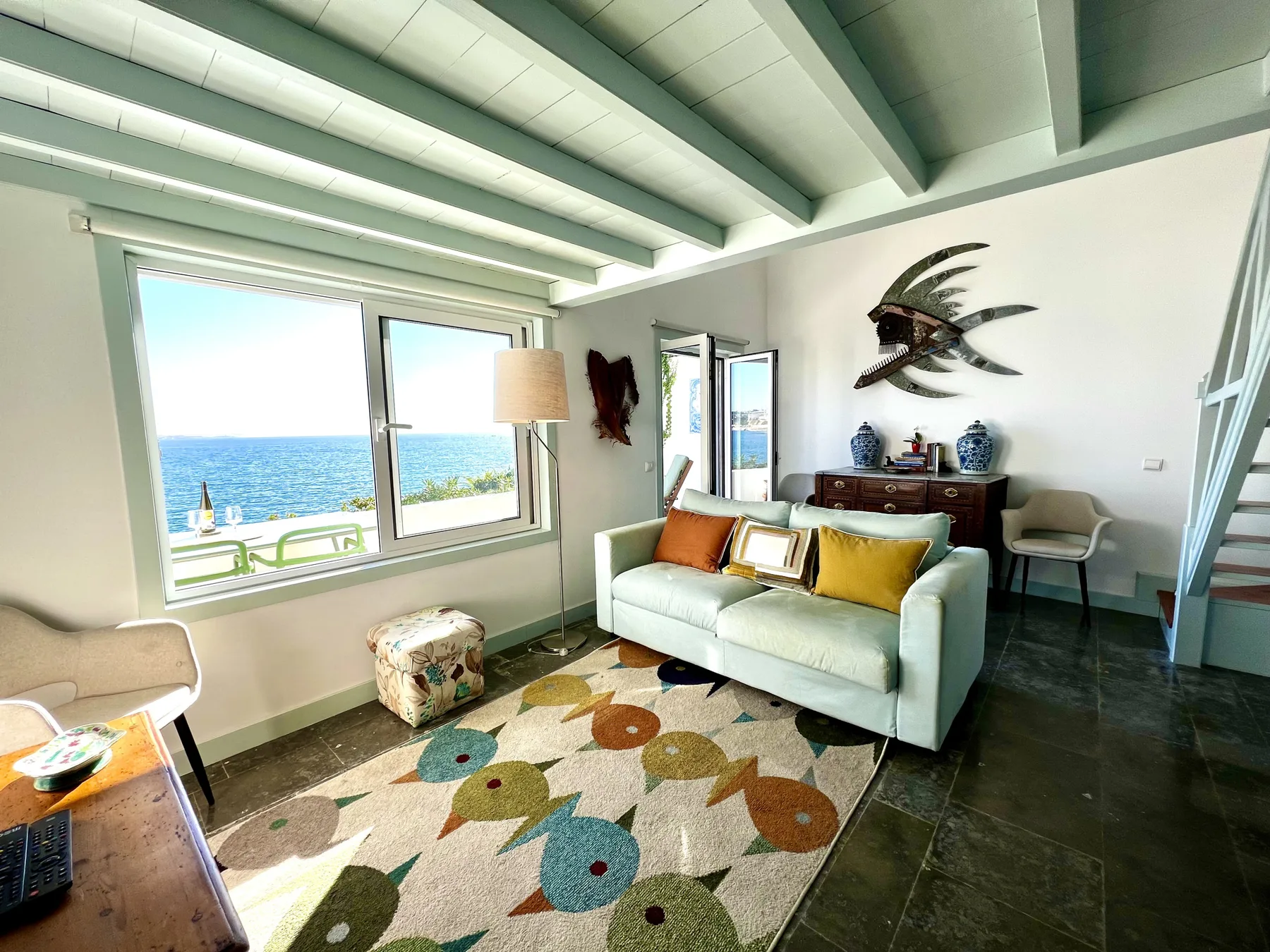 A bright living room with a sofa and large windows overlooking the sea.