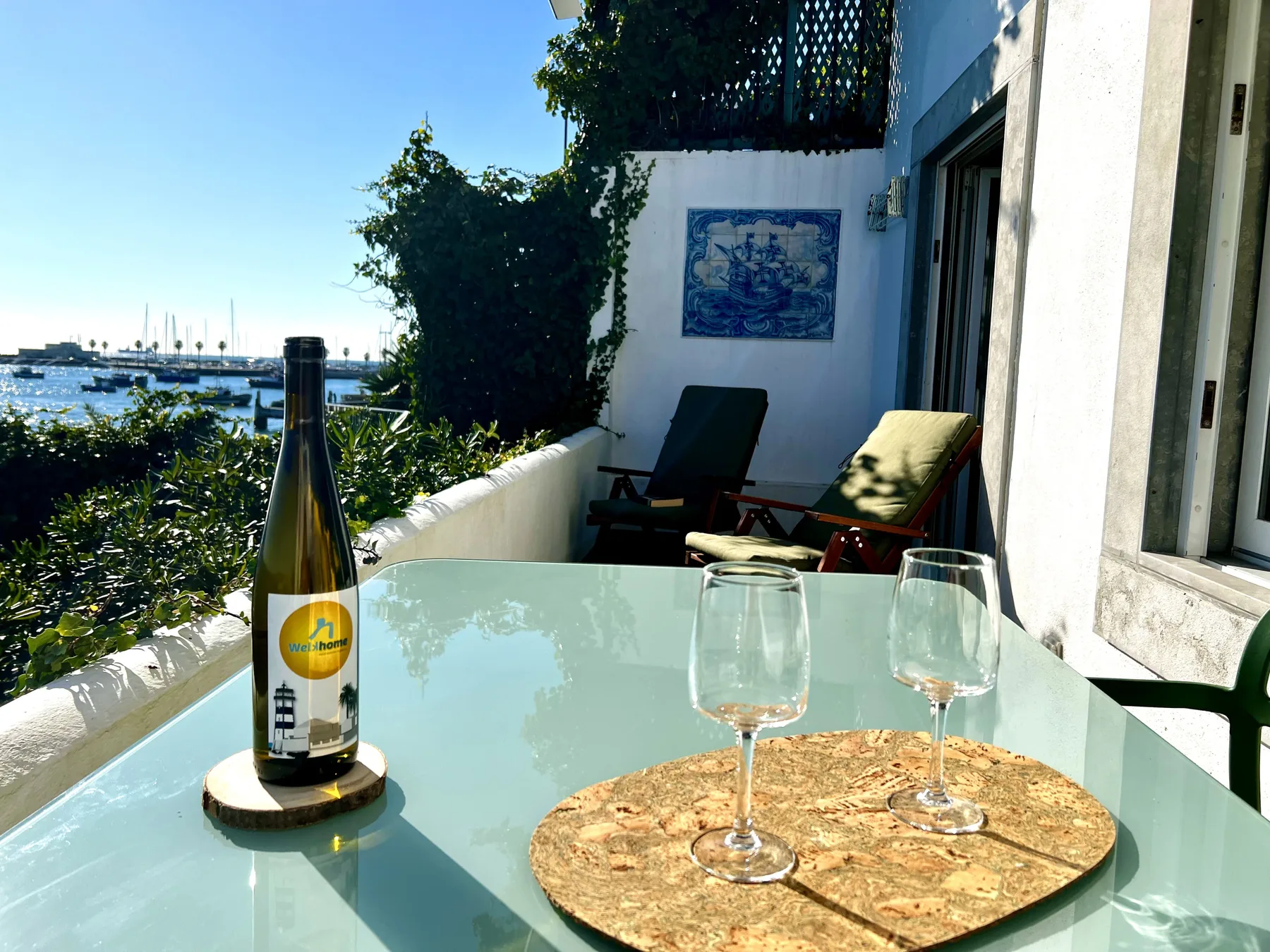 A waterfront balcony seating area with a glass table and views of boats.