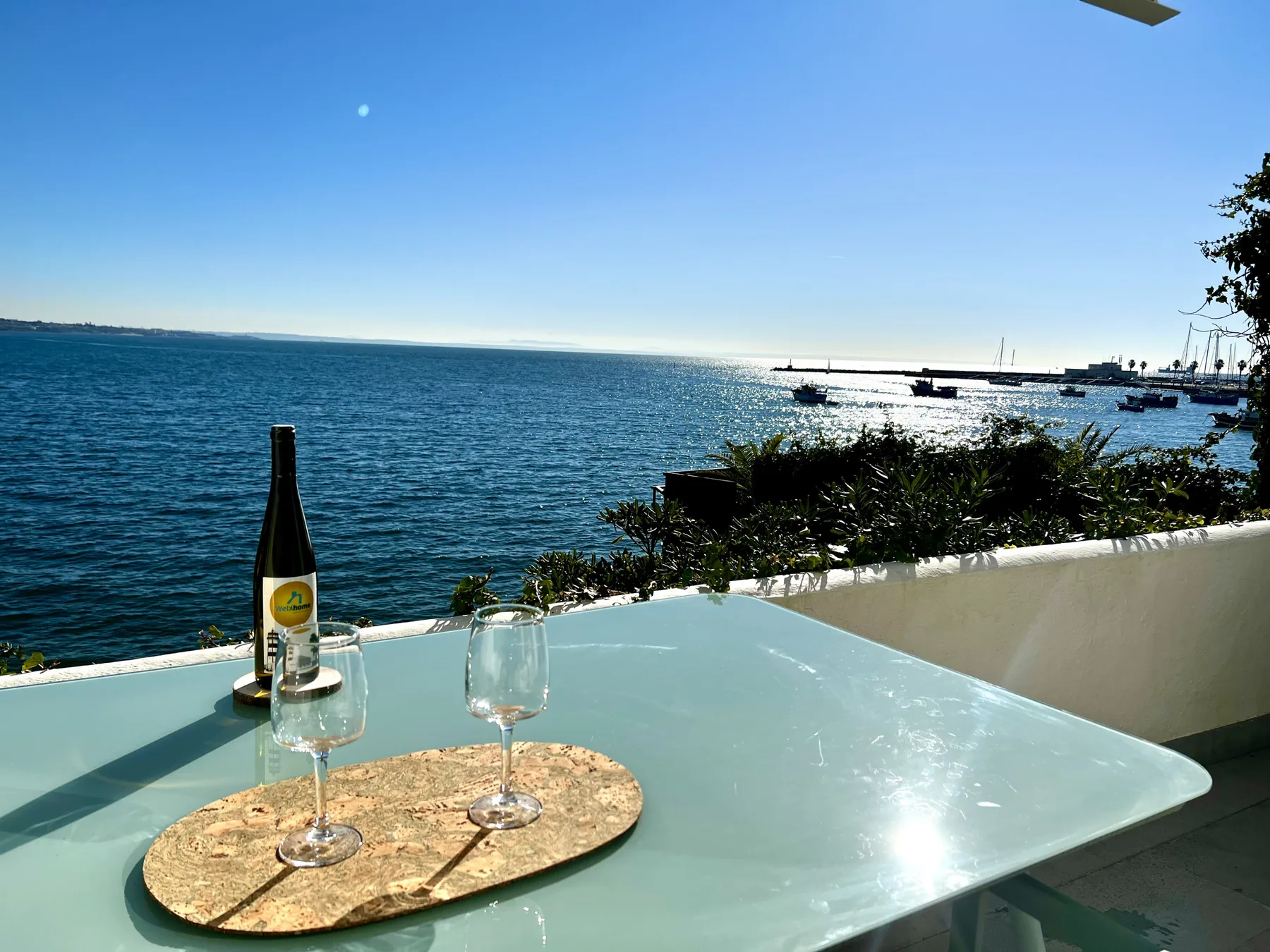 Una mesa en una terraza junto al mar ofrece vistas al agua, con una botella y copas.