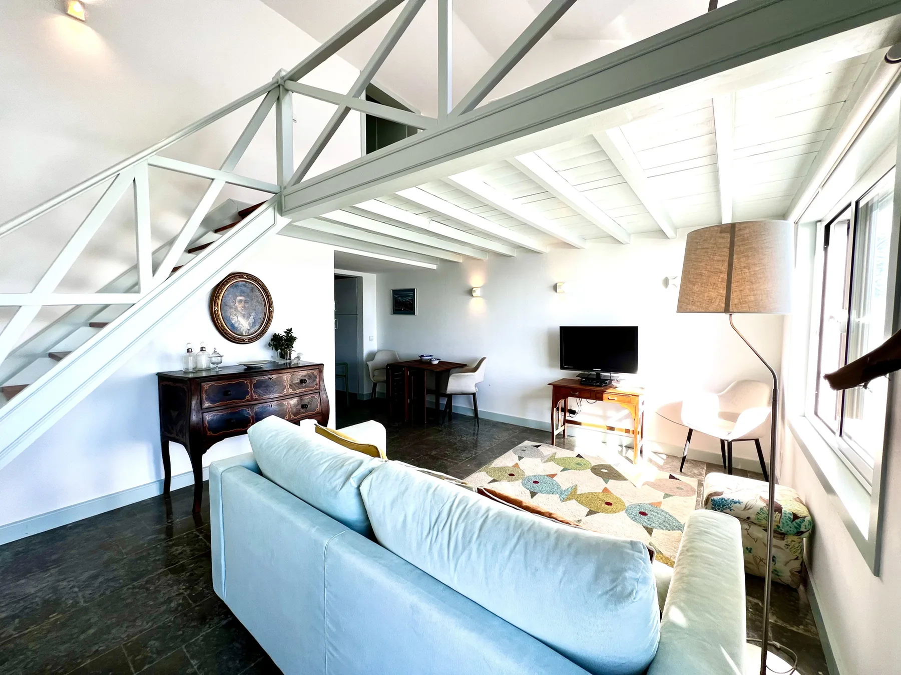 A bright living room with seating, a television, and an exposed staircase.