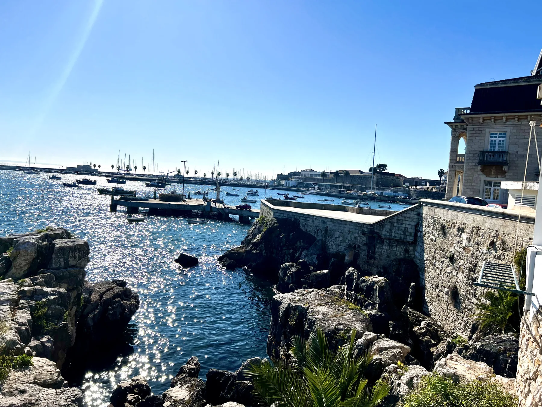 A coastal harbor with boats moored beyond rocky shoreline and stone walls.