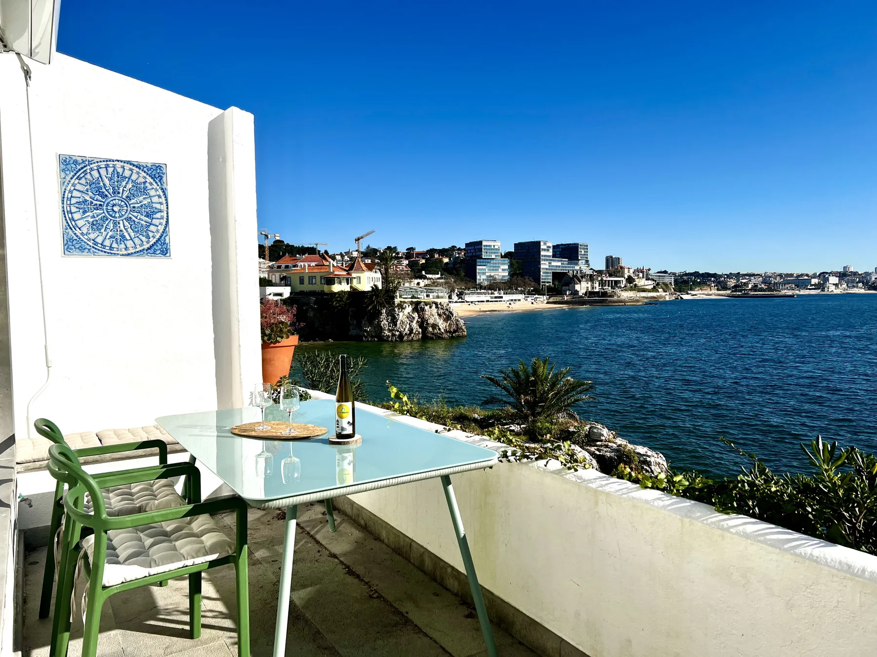A seaside terrace has a glass dining table and a view across the water.