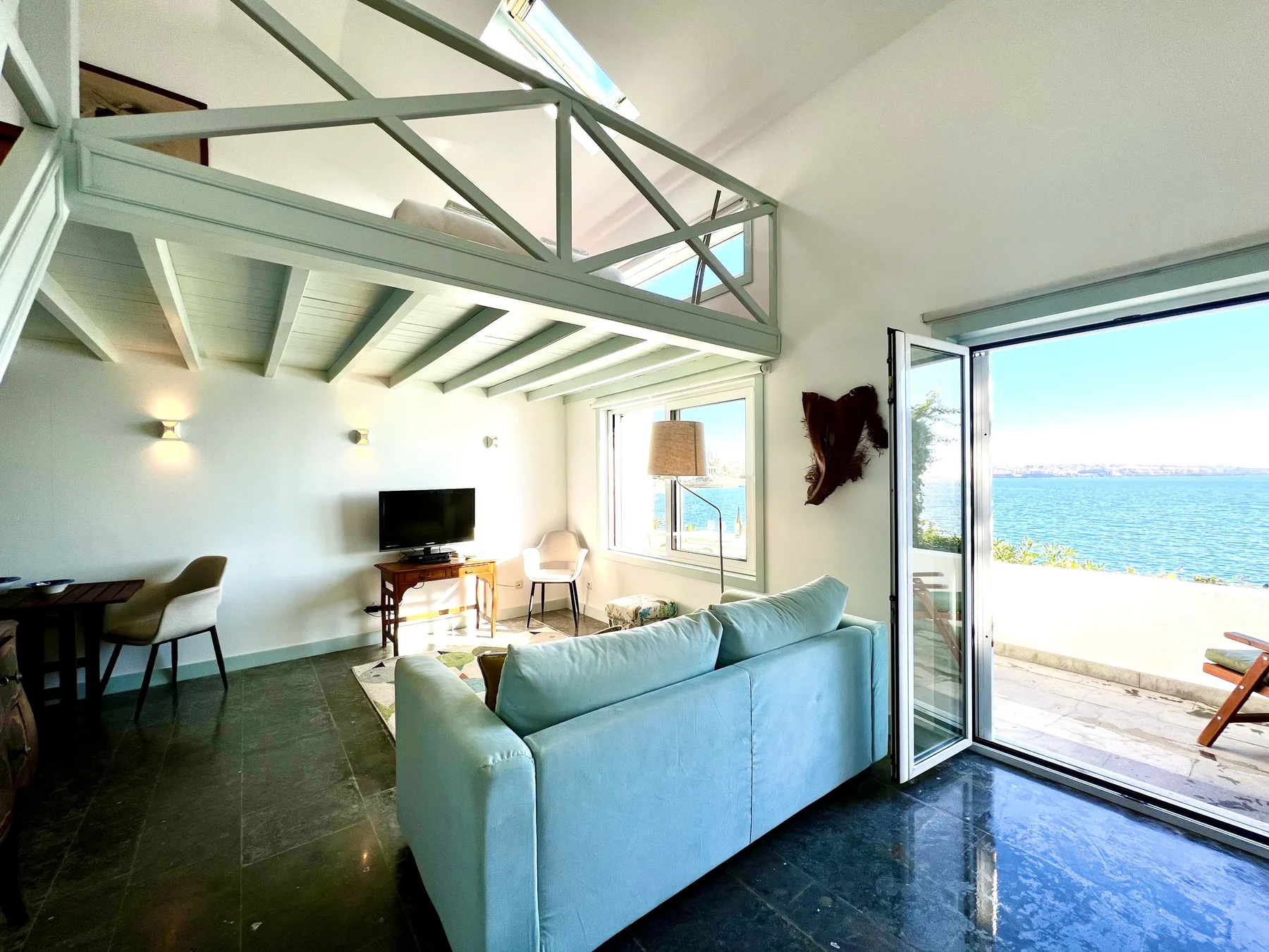 A bright living room opens onto a balcony overlooking the sea.