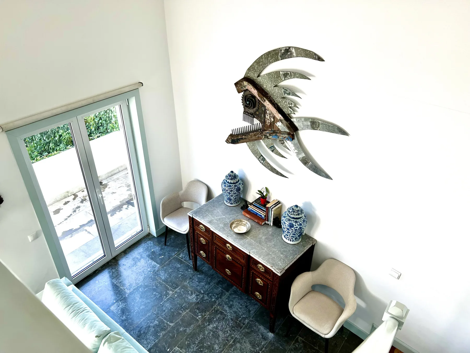 A bright living room has a dark floor, a wooden sideboard, and a sculptural wall decoration.