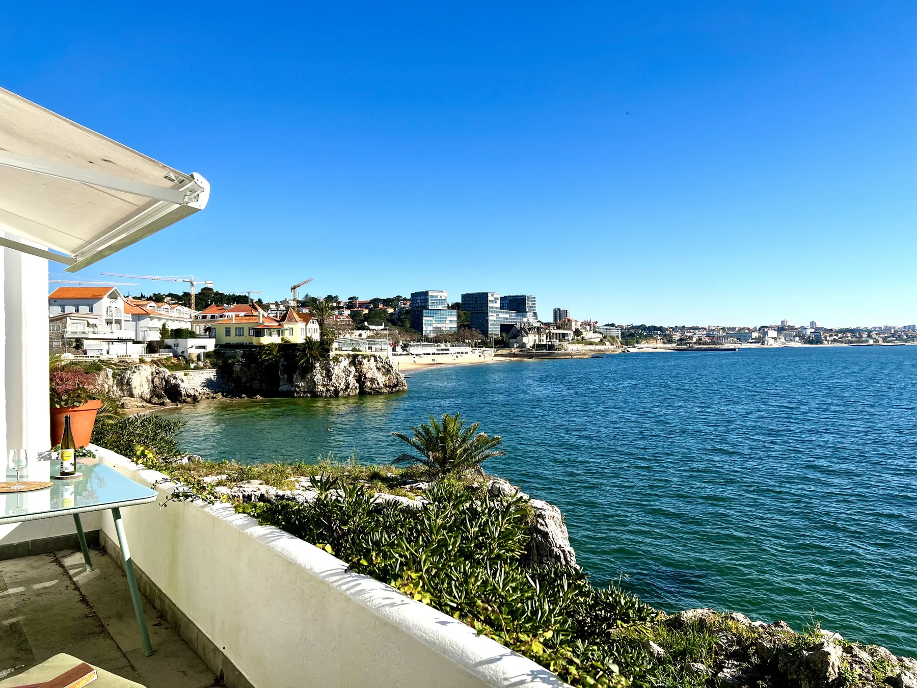 A seaside balcony overlooks the blue water and coastal buildings.