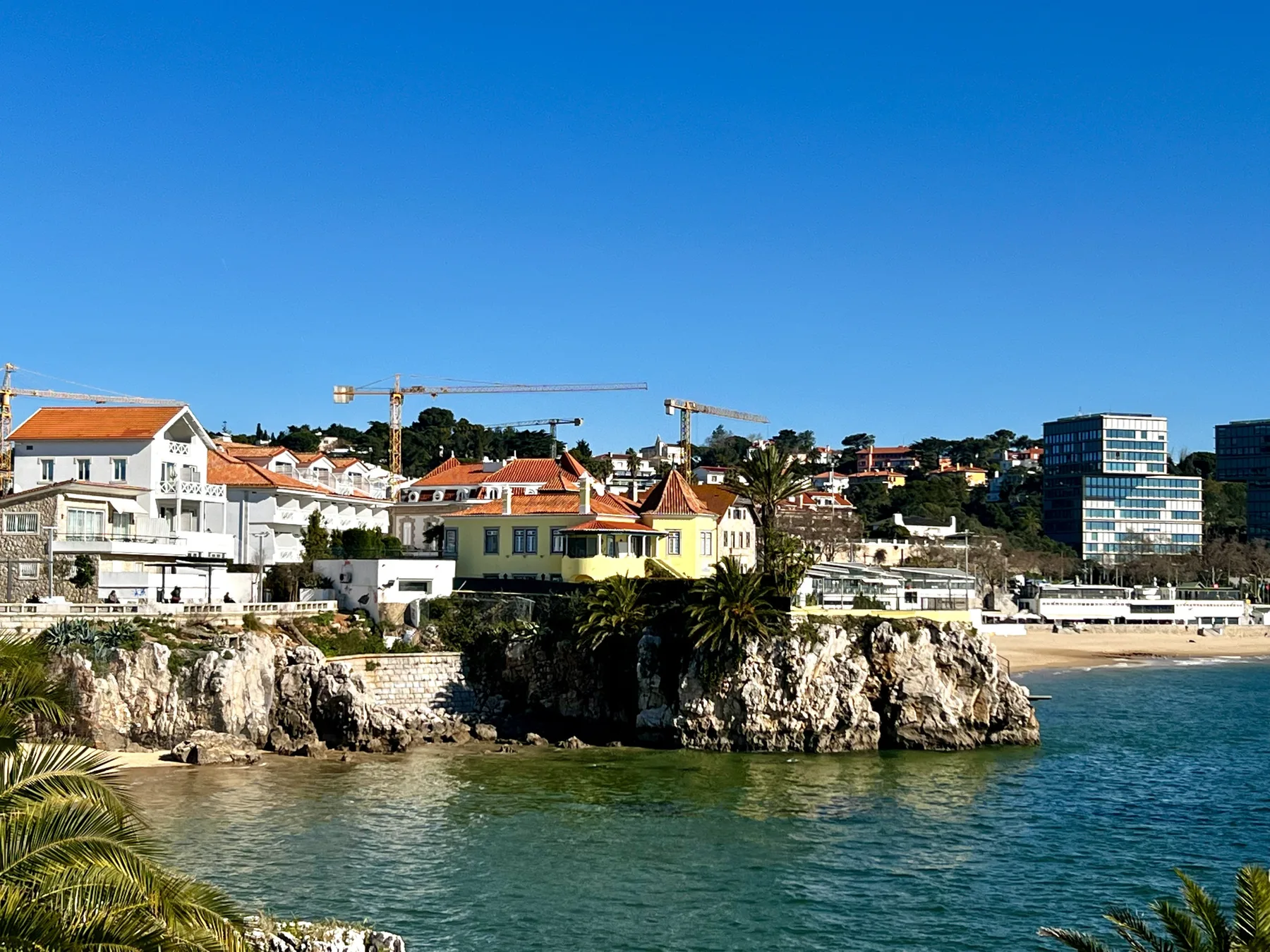 Coastal town buildings sit above rocky cliffs beside the sea.