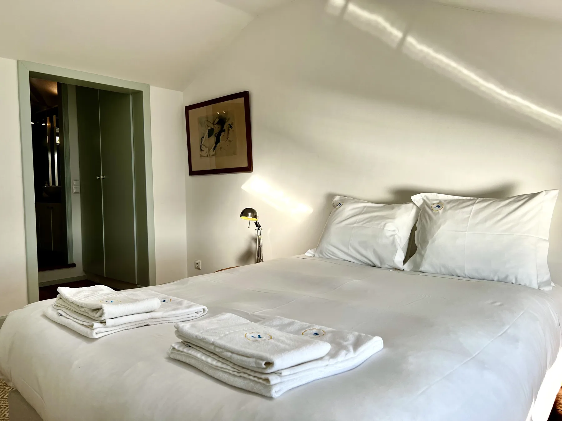 A bright bedroom with a neatly made bed and folded towels.