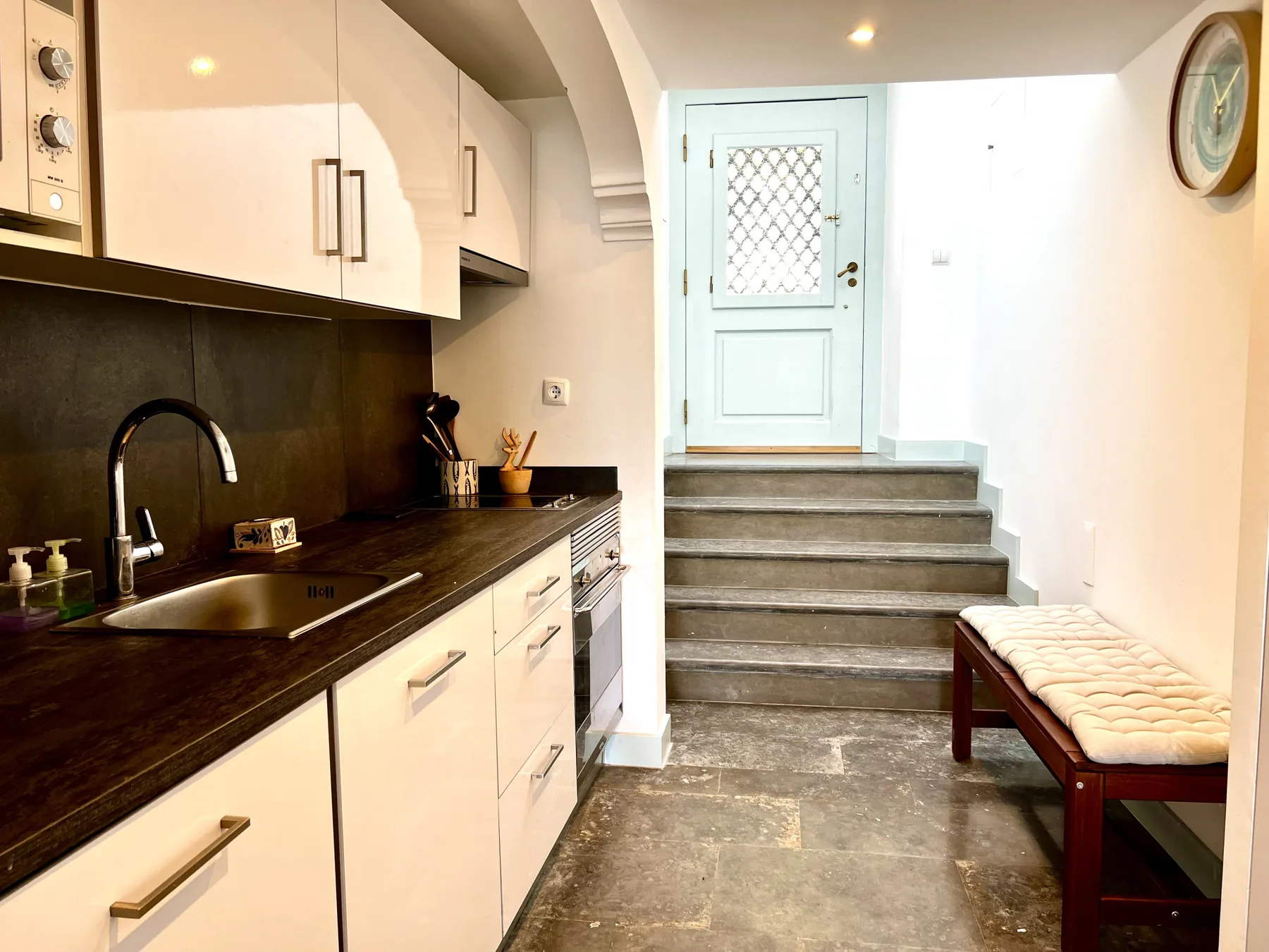 A kitchen with white cabinets and a dark countertop beside a raised entry.