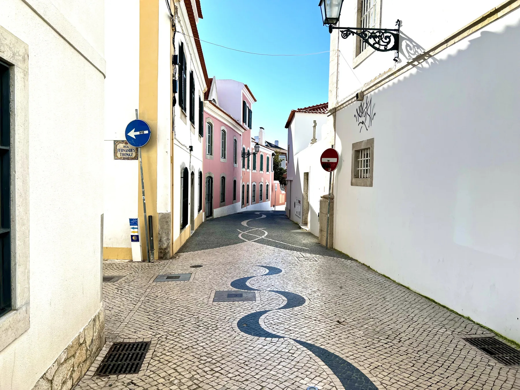 A narrow cobblestone street runs between white and pastel-colored buildings.