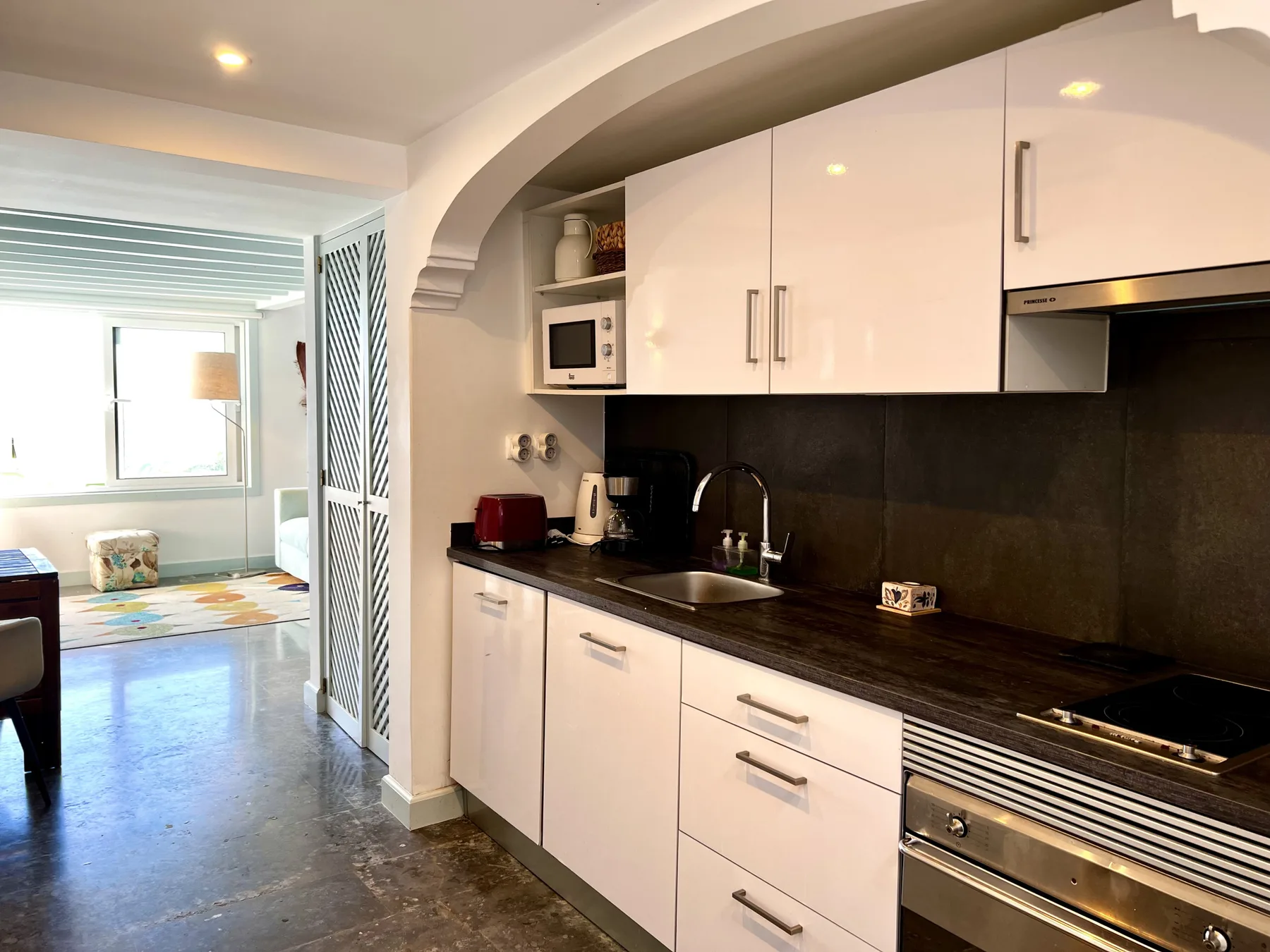 A compact kitchen with white cabinets, dark counters, and a stainless steel oven.