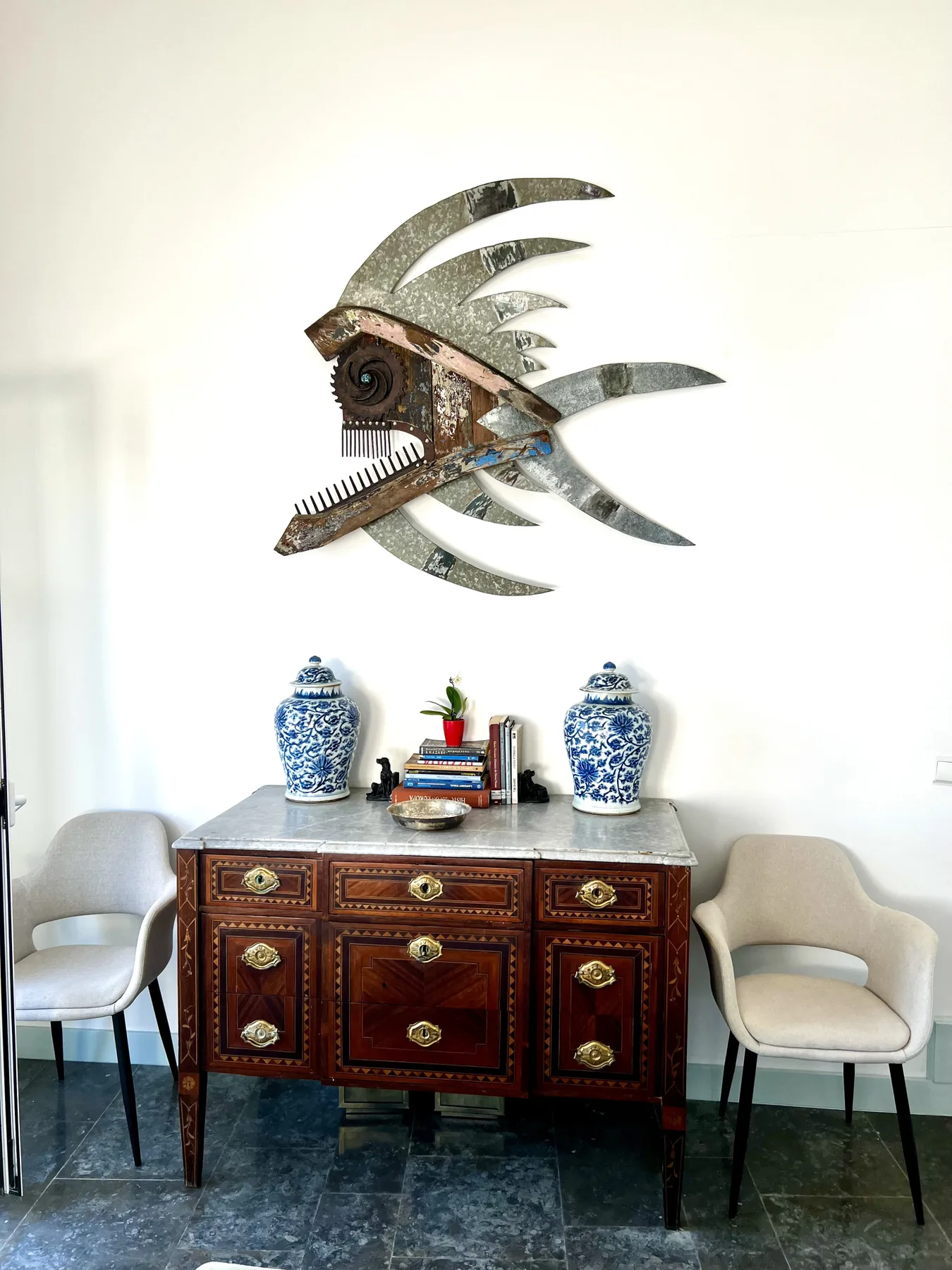 A dark wooden sideboard stands beneath a metal wall sculpture, with seating on either side.