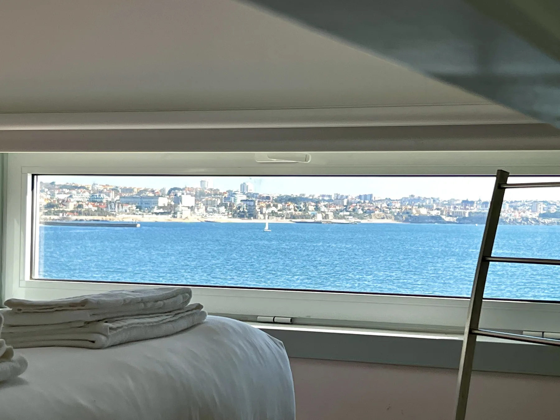 A bedroom with a bed beside a wide window overlooking the water.