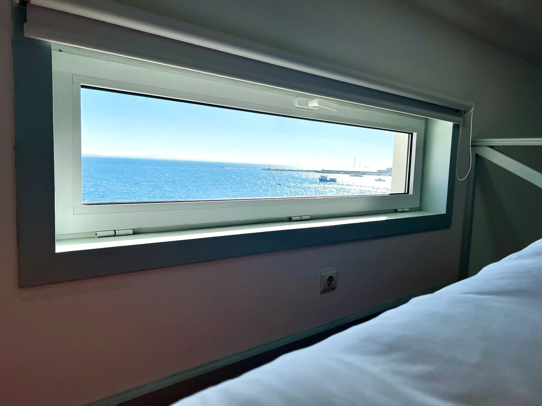 A bedroom with a narrow window overlooking the sea.