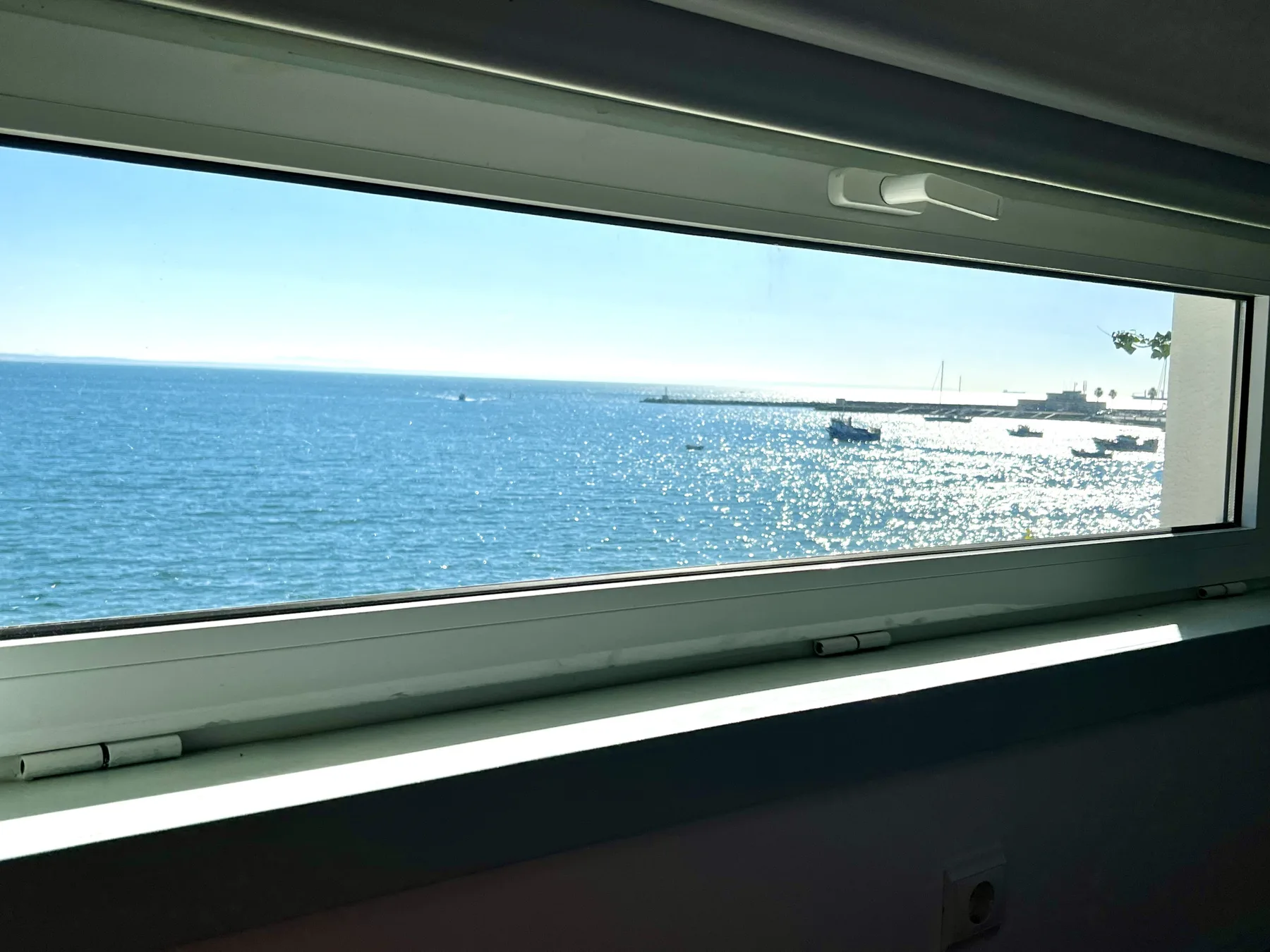 A narrow horizontal window frames a bright view of the sea.