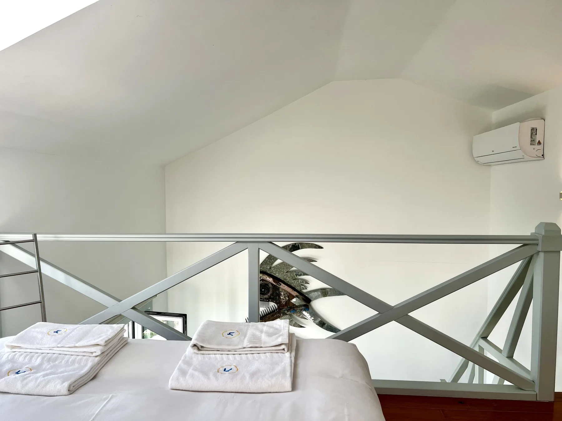 A loft sleeping area with a bed beneath a sloped ceiling and a metal railing.