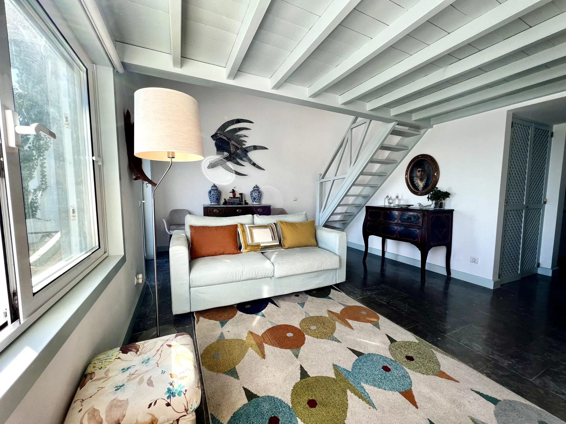 A bright living room with seating, a patterned rug, and a staircase.