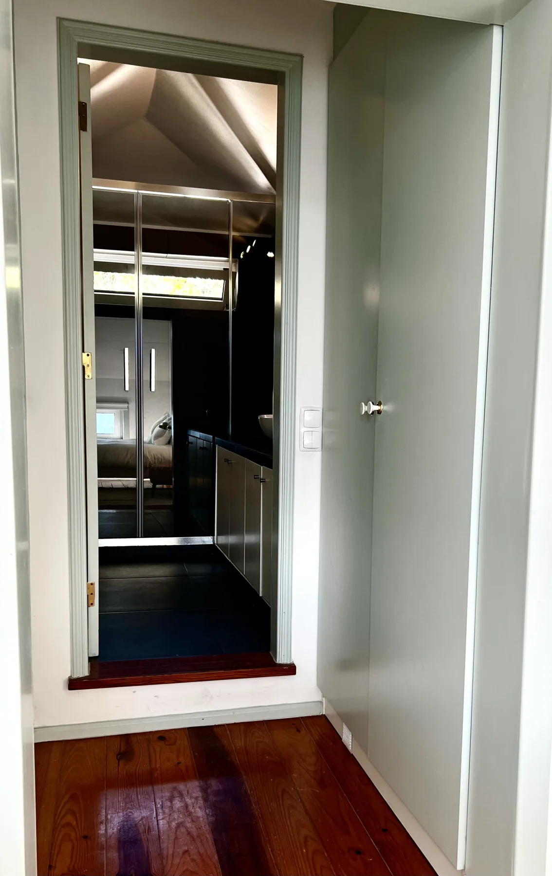 A hallway with wooden flooring leads to a bathroom with a shower.