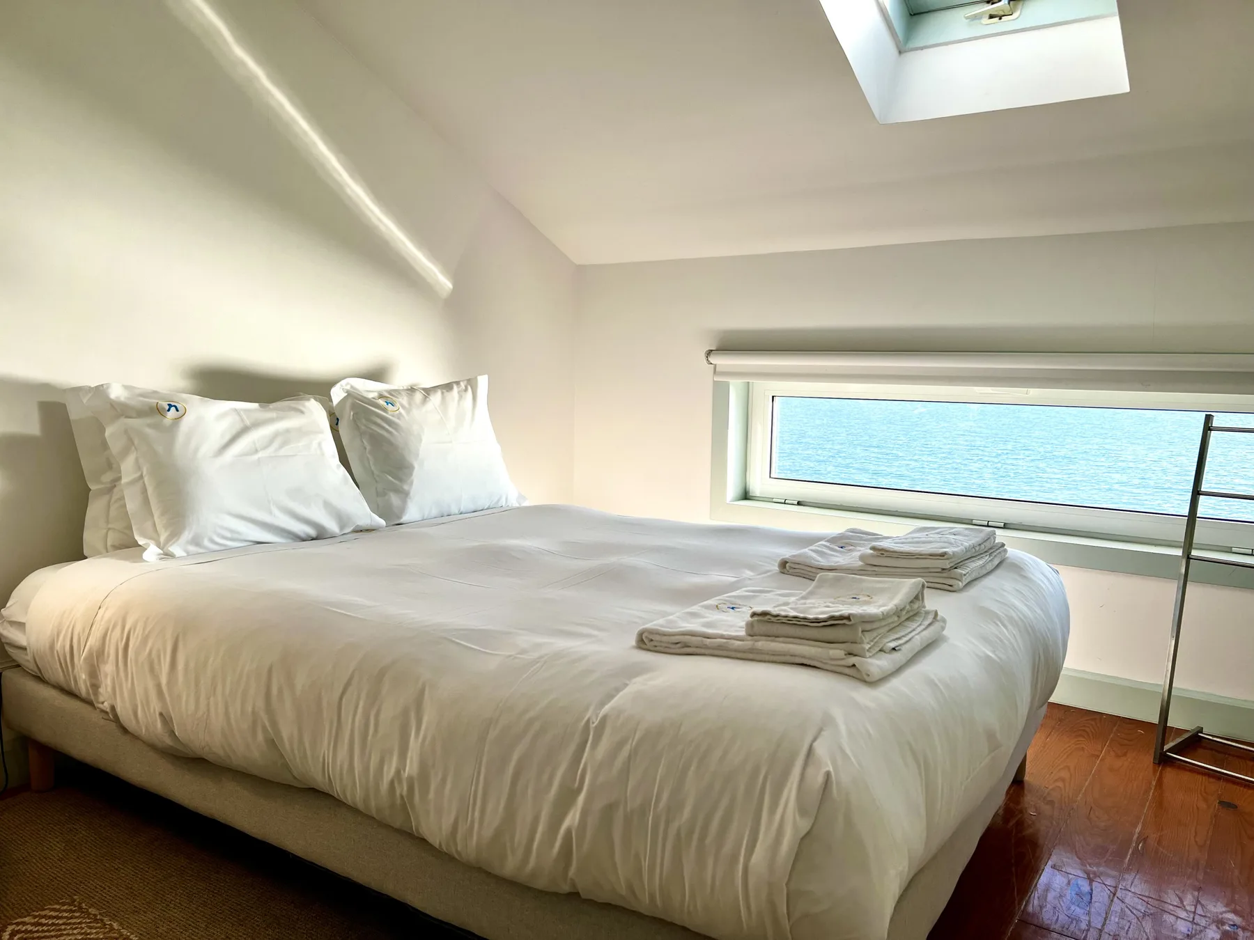 A bright bedroom has a neatly made bed beneath a sloped ceiling.