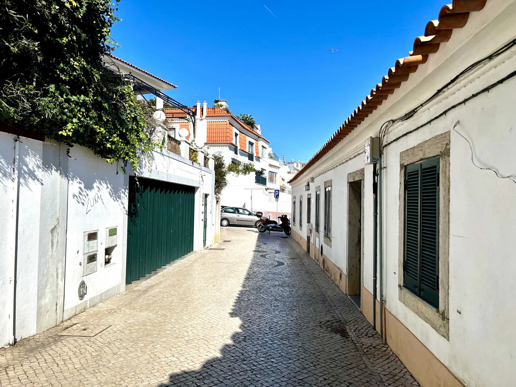 A narrow cobbled lane runs between white buildings under a clear blue sky.