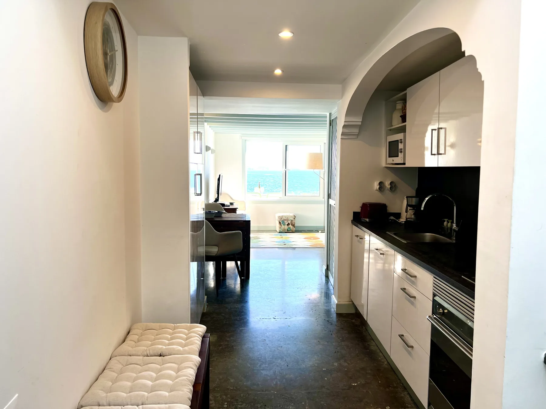 A kitchen opens onto a dining area and a bright room with a large window.