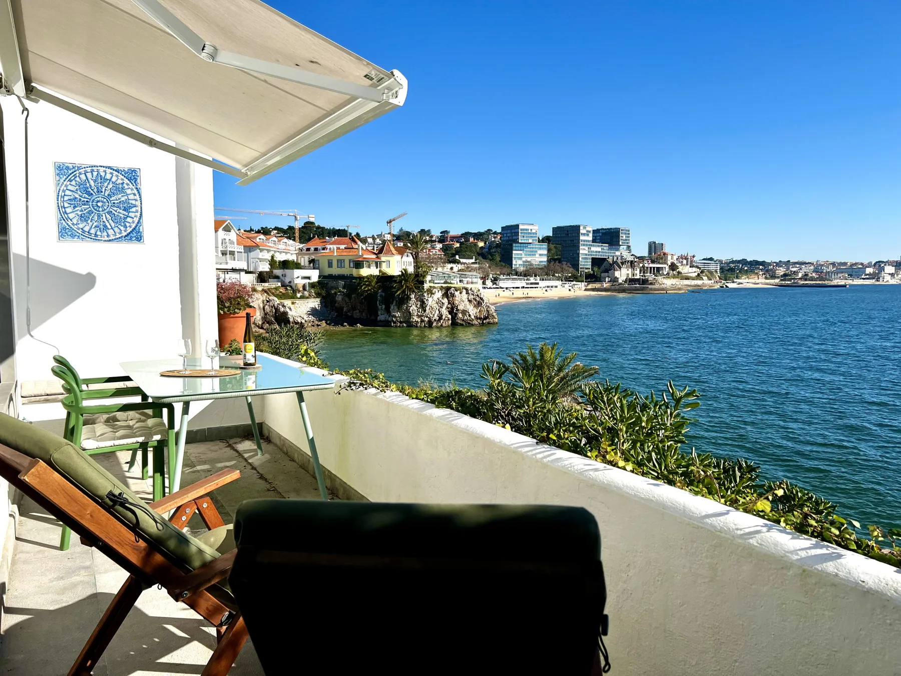 A seaside terrace overlooks the bay, with outdoor seating beneath a sunshade.