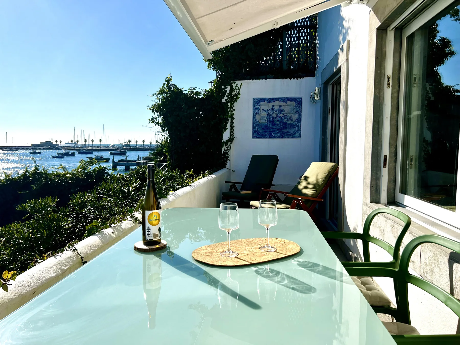 A waterfront patio has a glass table and seating overlooking boats in the harbor.