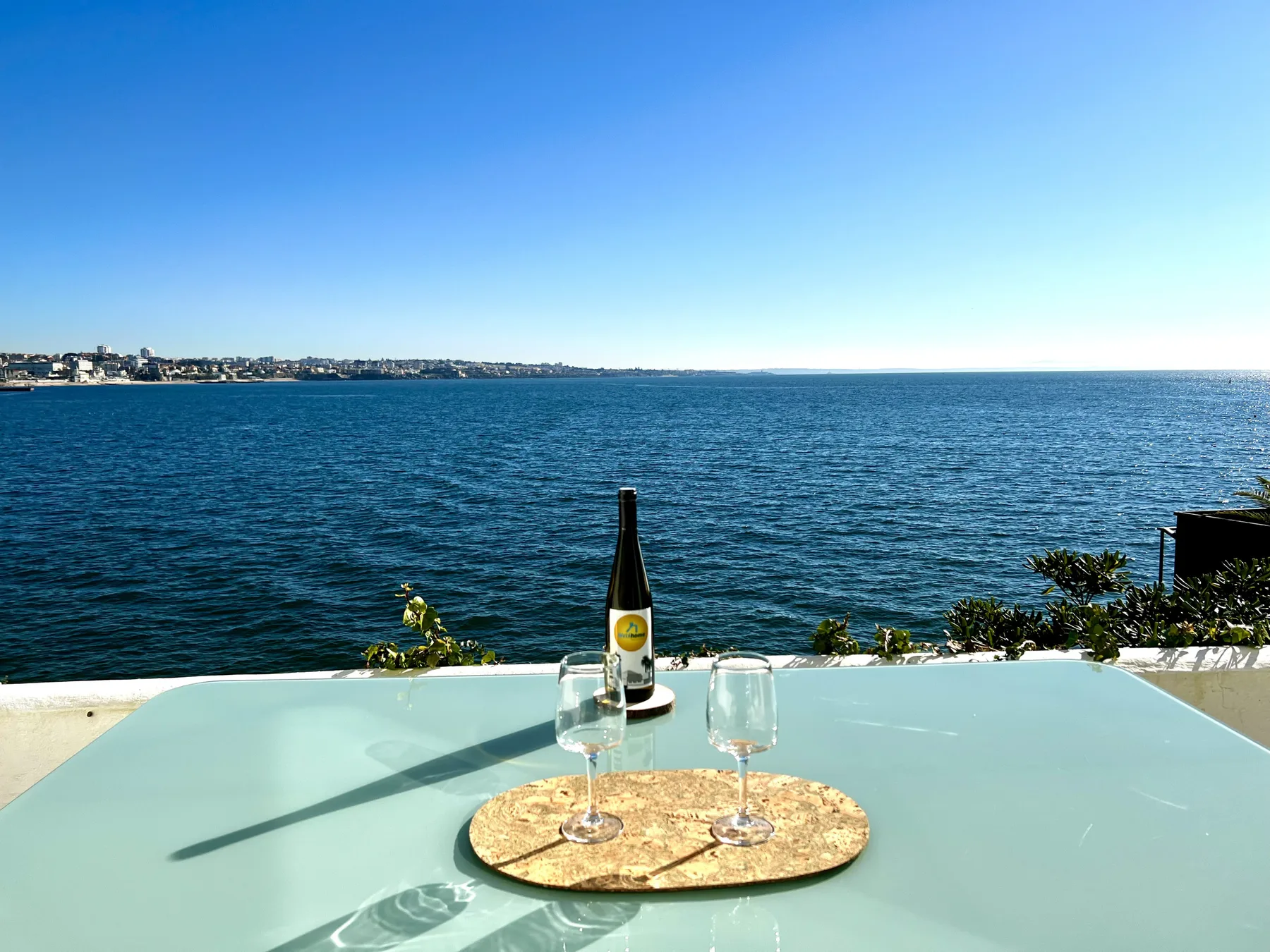 A waterfront table with a bottle and two glasses overlooks the sea.