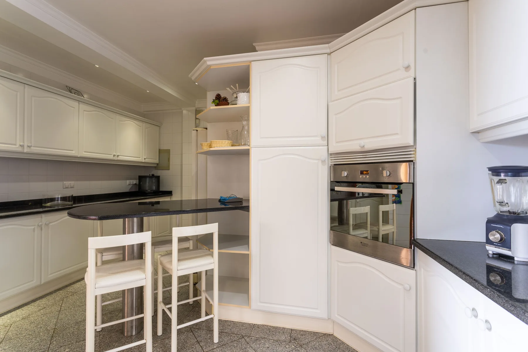 Una cocina luminosa con gabinetes blancos, una encimera y asientos de barra.