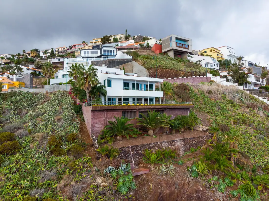 Un barrio en una ladera con casas, incluida una vivienda blanca rodeada de vegetación.