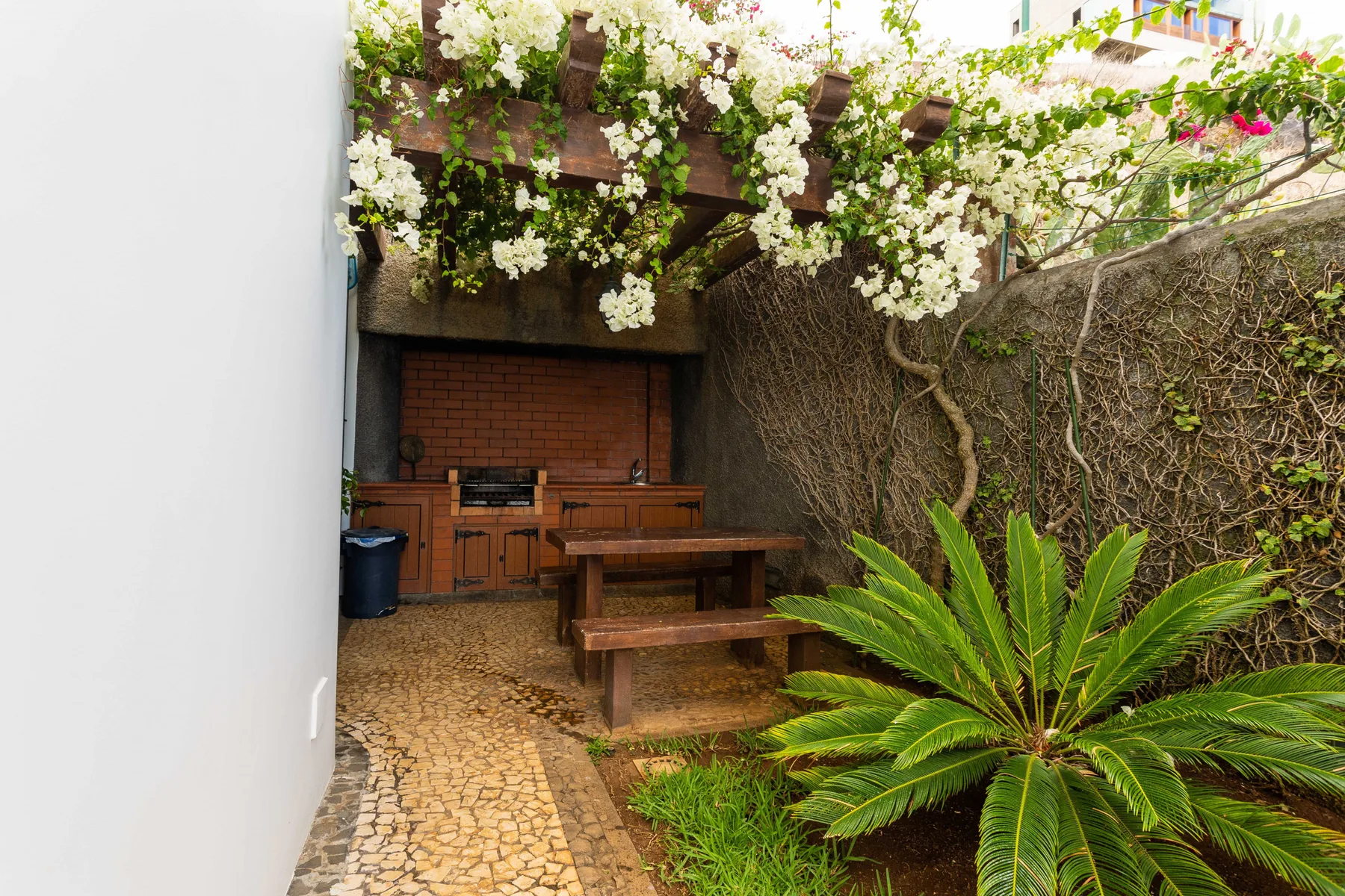 Un patio ajardinado con una mesa de madera bajo enredaderas en flor.