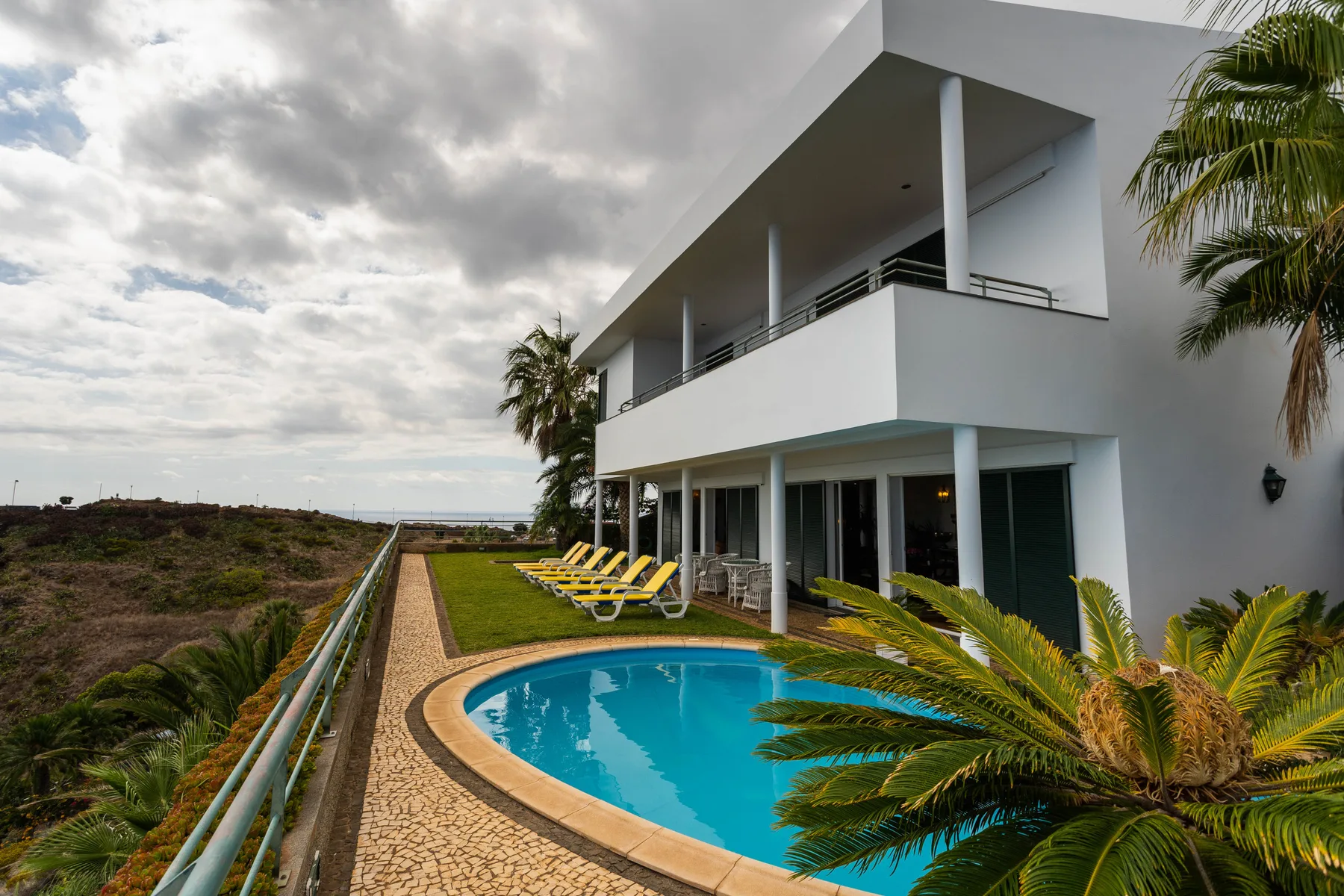 Una casa blanca moderna da a una piscina y varias tumbonas.