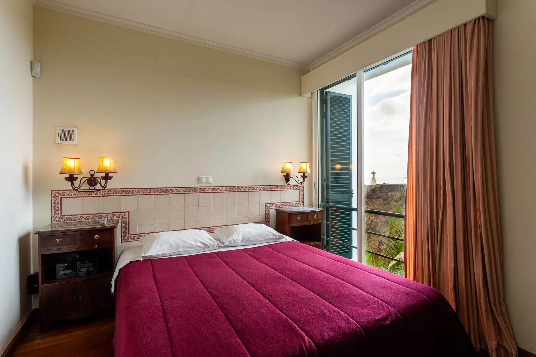 Un dormitorio con una colcha magenta y puertas abiertas al balcón.