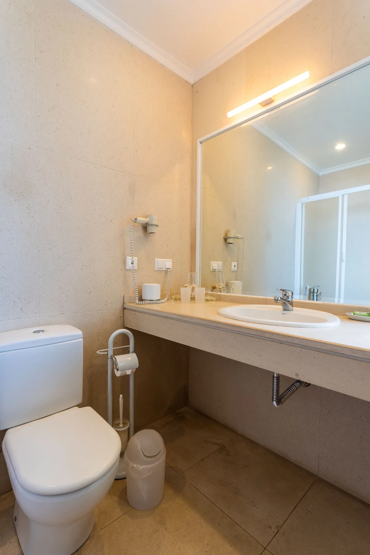 Un baño con un inodoro junto a un largo tocador y un espejo.