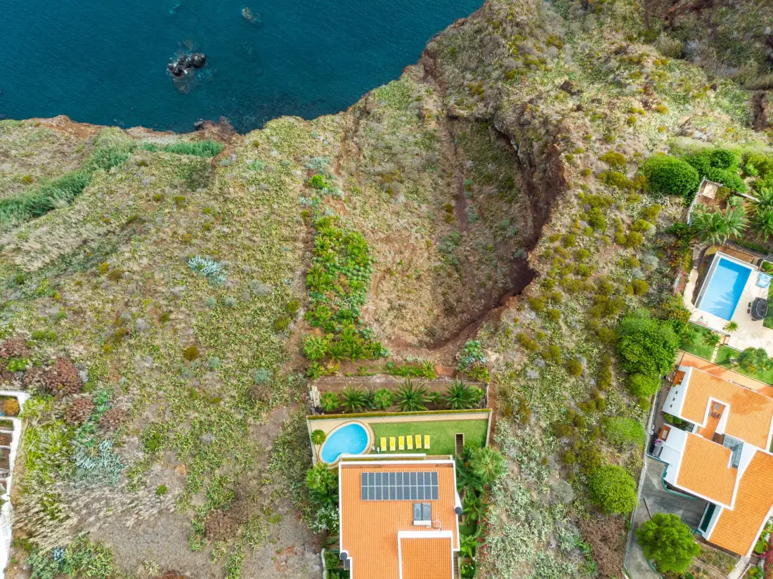 Una vista aérea muestra viviendas y piscinas junto a terreno rocoso y el mar.