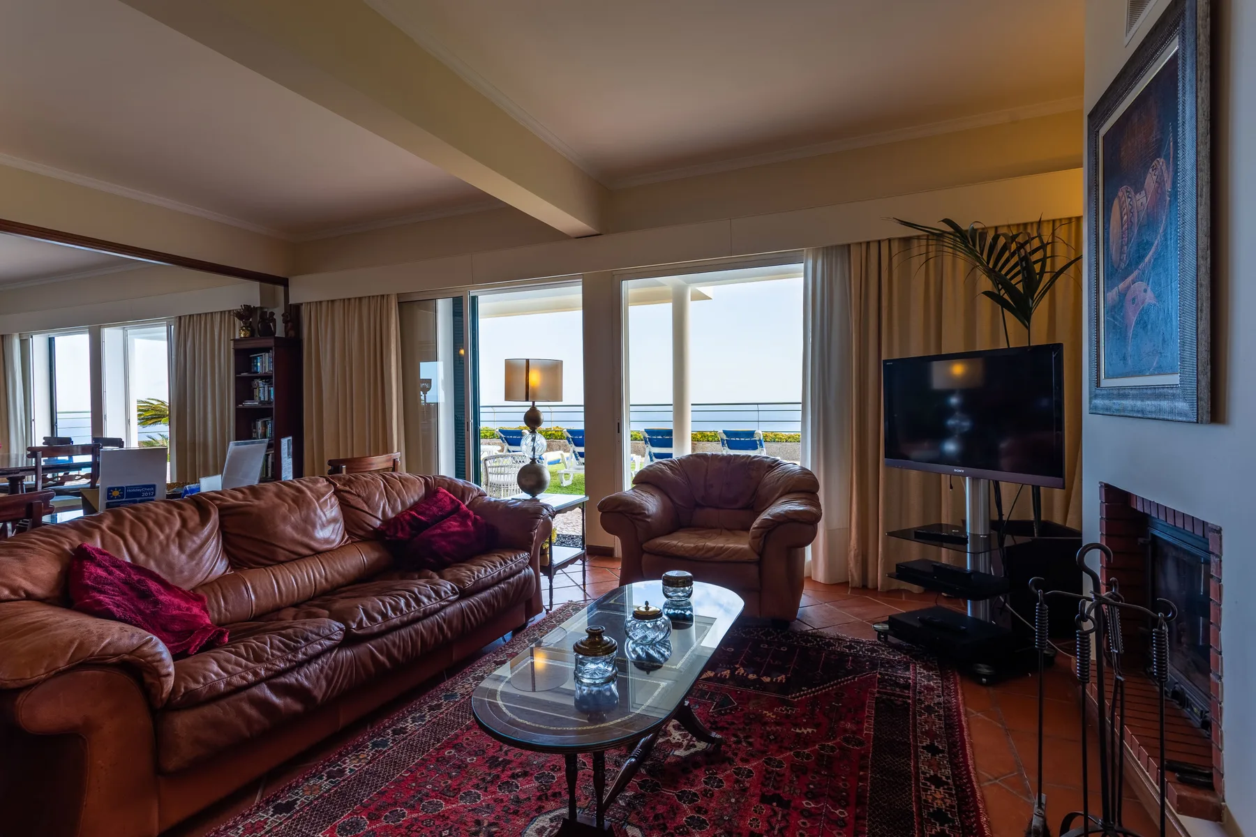Una sala de estar con asientos, un televisor y amplias puertas de cristal hacia el mar.