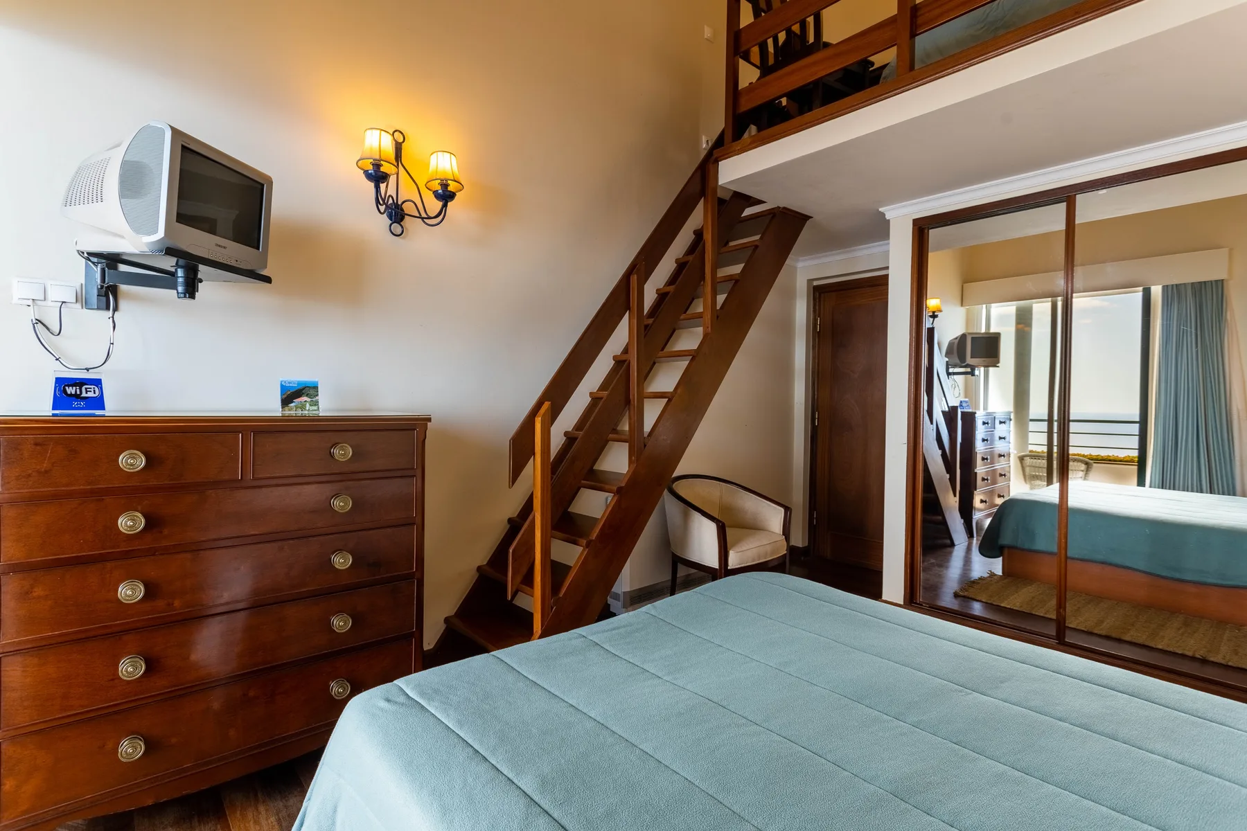 Un dormitorio con una cama, una cómoda de madera y una escalera hacia un nivel superior.