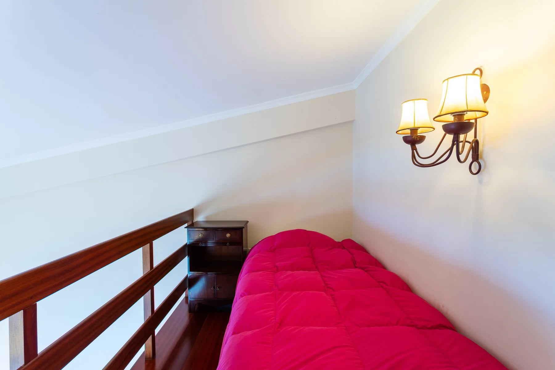 A compact sleeping area with a bright pink quilt and a wooden railing.